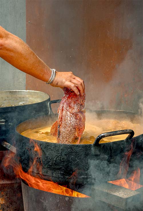 La bouillabaisse au feu de bois de L'Aventure — restaurant de plage à Carqueiranne Cuisson de la bouillabaisse au feu de bois au restaurant L'Aventure à Carqueiranne — poisson frais plongé à la main dans le bouillon